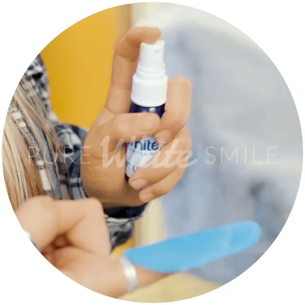 A client applying teeth whitening activation spray to a disposable finger wipe before gently applying it to their teeth as part of step 3 of the laser teeth whitening process at Pure White Smile in Chorley.